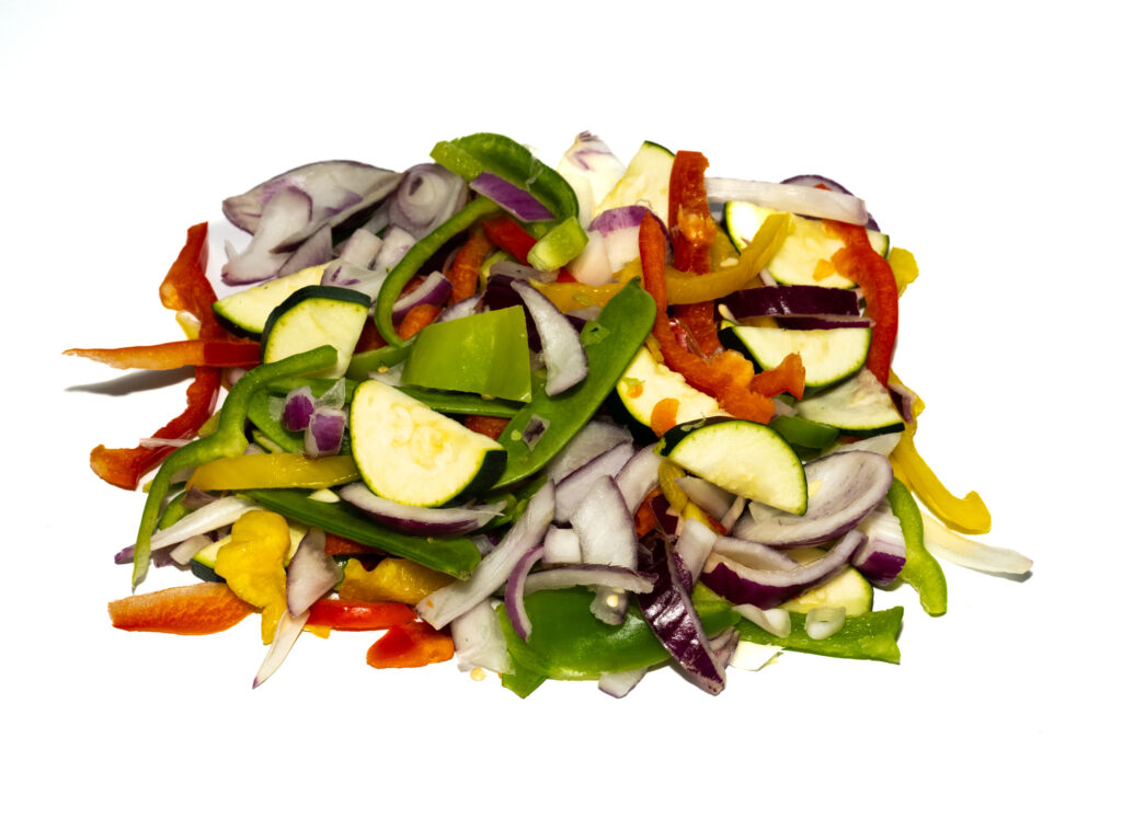 A mix of sliced vegetables including green bell peppers, red bell peppers, yellow bell peppers, red onions, and zucchini