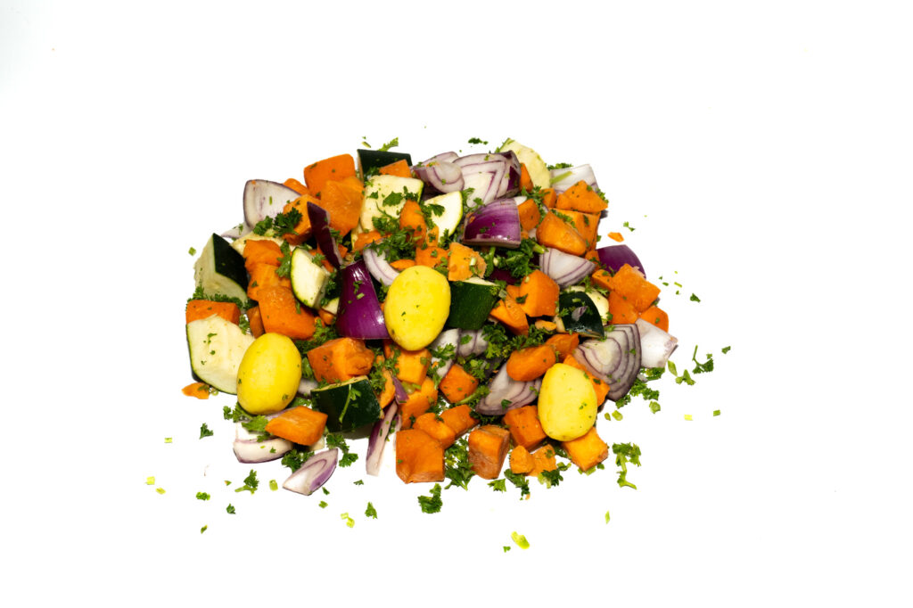 chopped vegetables including orange sweet potatoes, yellow baby potatoes, red onions, and green zucchini, garnished with fresh parsley