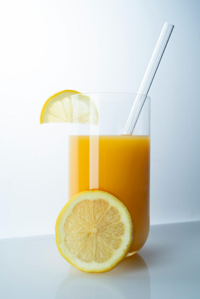 A glass of orange juice garnished with slices of orange and served with glass straw