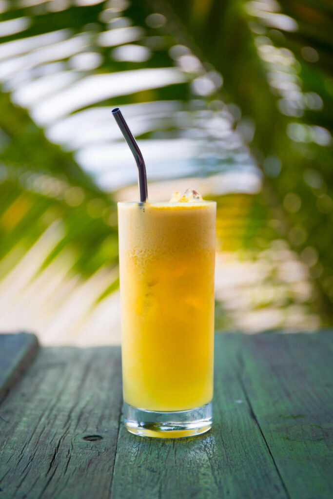 A glass of fresh orange juice with ice and a metal straw on a tropical background